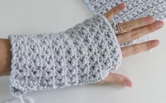 a woman's hand holding onto a crocheted gray wrist warmer on top of a white table