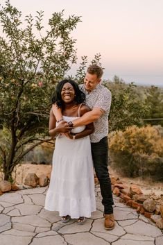 a man and woman hugging each other in front of an apple tree