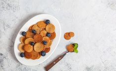 a white plate topped with pancakes and blueberries next to a knife on a table