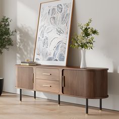 a wooden cabinet with two drawers next to a potted plant and a framed print on the wall