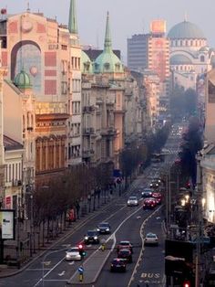 a city street filled with lots of traffic next to tall buildings on either side of the road