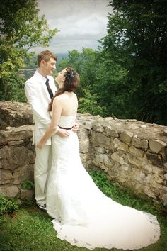 a bride and groom standing next to each other in front of a stone wall on their wedding day