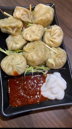 some dumplings and sauce on a black plate