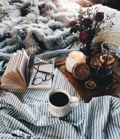 an open book, cup of coffee and eyeglasses on a bed with blankets