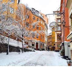 a snowy street with buildings and people walking in the snow on it's sides