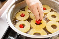 a person placing pineapples on top of some fruit in a pot with water