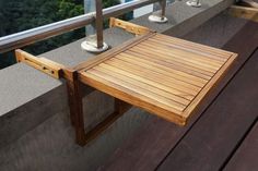 a wooden table sitting on top of a balcony next to a metal pole and railing