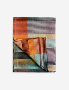 a multicolored checkered blanket folded on top of a white surface with an orange and black stripe