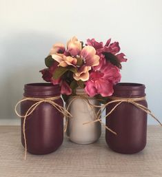 three jars with flowers in them sitting on a table next to some string and twine