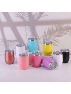 thermos are lined up in different colors and sizes, with palm leaves behind them