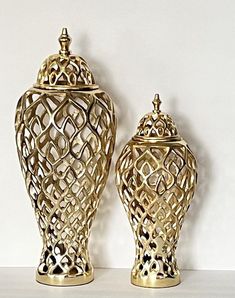 two gold vases sitting next to each other on a white counter top in front of a wall