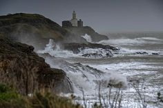 waves crashing against the rocks and lighthouses on an overcast day