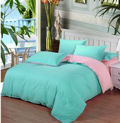 a bed with blue and pink comforters in a room next to a plant on the floor