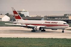 a red and white plane is on the runway at an airport with buildings in the background