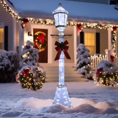 a street light decorated with christmas lights in front of a white house covered in snow