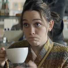 a woman holding a coffee cup in her right hand and looking at the camera with an upset look on her face