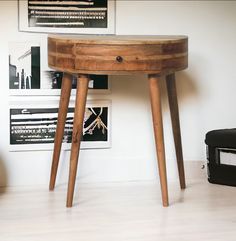 a small wooden table with two legs in front of a white wall and pictures on the wall