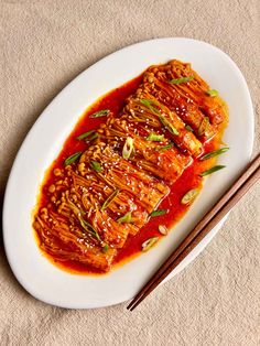 a white plate topped with meat covered in sauce and chopsticks next to it