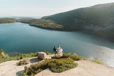 a man and woman standing on top of a mountain next to a lake