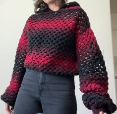 a woman wearing a red and black crochet sweater standing in front of a white wall