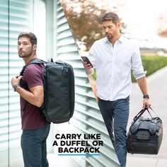 two men walking down the street with luggage and cell phones in their hands, one carrying a duffle bag