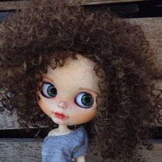 a close up of a doll with big blue eyes and curly hair on a bench