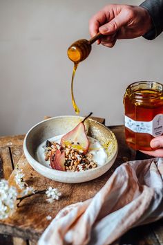 a person is pouring honey into a bowl of oatmeal and apple slices