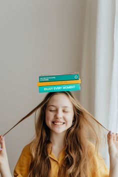 a girl with long hair holding three books on top of her head and smiling at the camera