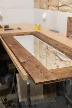 an unfinished table is being worked on with wood and glass in the center, along with other workbench tools