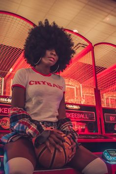 a woman sitting on top of a basketball ball in front of a red neon sign