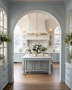 an archway leads into a kitchen with blue cabinets and white counter tops, along with flowers in vases on the island