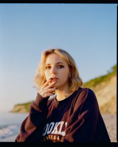 a woman sitting on the beach with her hand in her mouth and looking at the camera