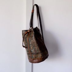 Discover this unique, handmade vintage leather backpack, crafted from soft, high-quality Moroccan leather. Featuring an intricate, abstract ethnic pattern, this bucket-style bag is both stylish and functional. The bag's natural patina, developed over time, adds a touch of vintage charm. The soft, supple leather is dyed with natural colors, creating a stunning palette of browns and greens. Key Features: Handmade in Morocco: Crafted with care and attention to detail. High-Quality Leather: Durable Vintage Bucket-shape Travel Bag, Vintage Bucket Travel Bag, Vintage Leather Bucket Bag, Vintage Brown Tote Bucket Bag, Vintage Brown Bucket Bag, Vintage Bucket Bag For Travel, Traditional Bucket Bag With Adjustable Strap For Everyday, Vintage Bucket Shape Shoulder Bag For Daily Use, Artisan Brown Backpack Shoulder Bag