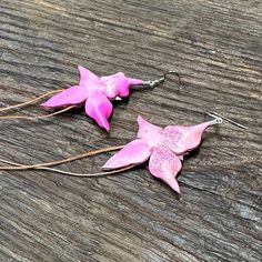 two pink flowers are sitting on the wooden table next to each other, with long metal ear wires