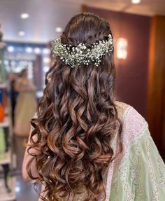 the back of a woman's head with long curly hair and flowers in her hair