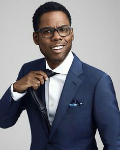 a man in a blue suit and glasses is straightening his tie with the help of a pair of scissors