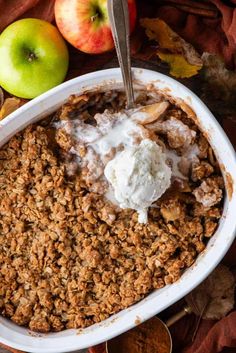 an apple crisp in a white bowl with ice cream and two apples on the side