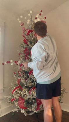 a man decorating a christmas tree with red, white and blue decorations on it