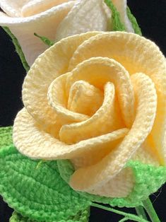 two crocheted roses with green leaves on the stems, one yellow and one white