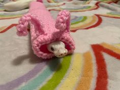 a small pink stuffed animal laying on top of a colorful bed sheet with rainbow stripes