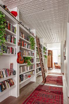 a living room filled with lots of books and furniture next to a long book shelf