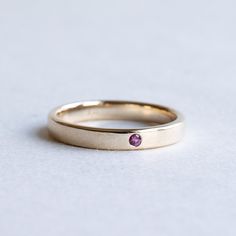 a yellow gold band with a single pink sapphire stone in the center, sitting on a white surface