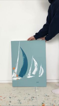 a person holding up a painting with sailboats on it