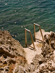 two metal railings sticking out of the rocks by the water's edge, with an ocean in the background