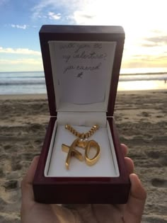 a person holding up a gold necklace in front of the ocean