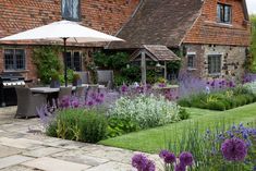 an outdoor garden with purple flowers and lavenders in the foreground, next to a brick building