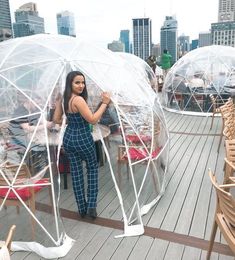 a woman standing in a clear bubble tent on top of a wooden deck next to tables and chairs