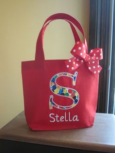 a red tote bag with a polka dot bow on the front and letter s on the back