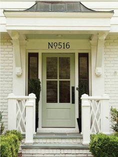 the front door of a white house with black shutters and two plants on either side