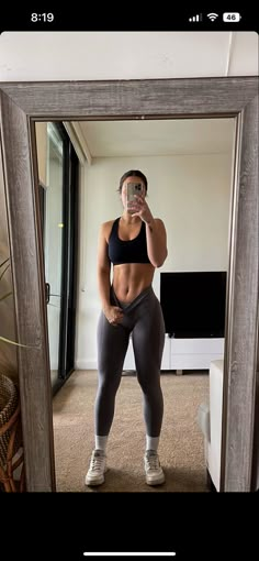 a woman taking a selfie in front of a mirror wearing leggings and sports bra